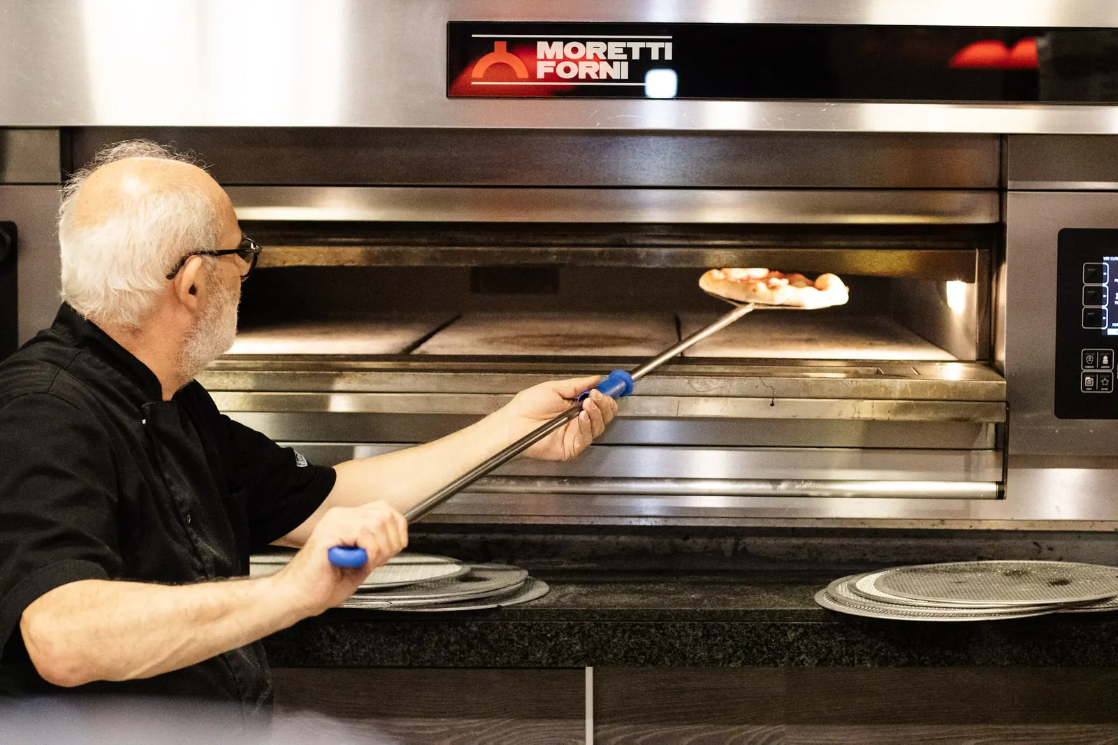 Il pizzaiolo inforna una pizza con la pala nel forno